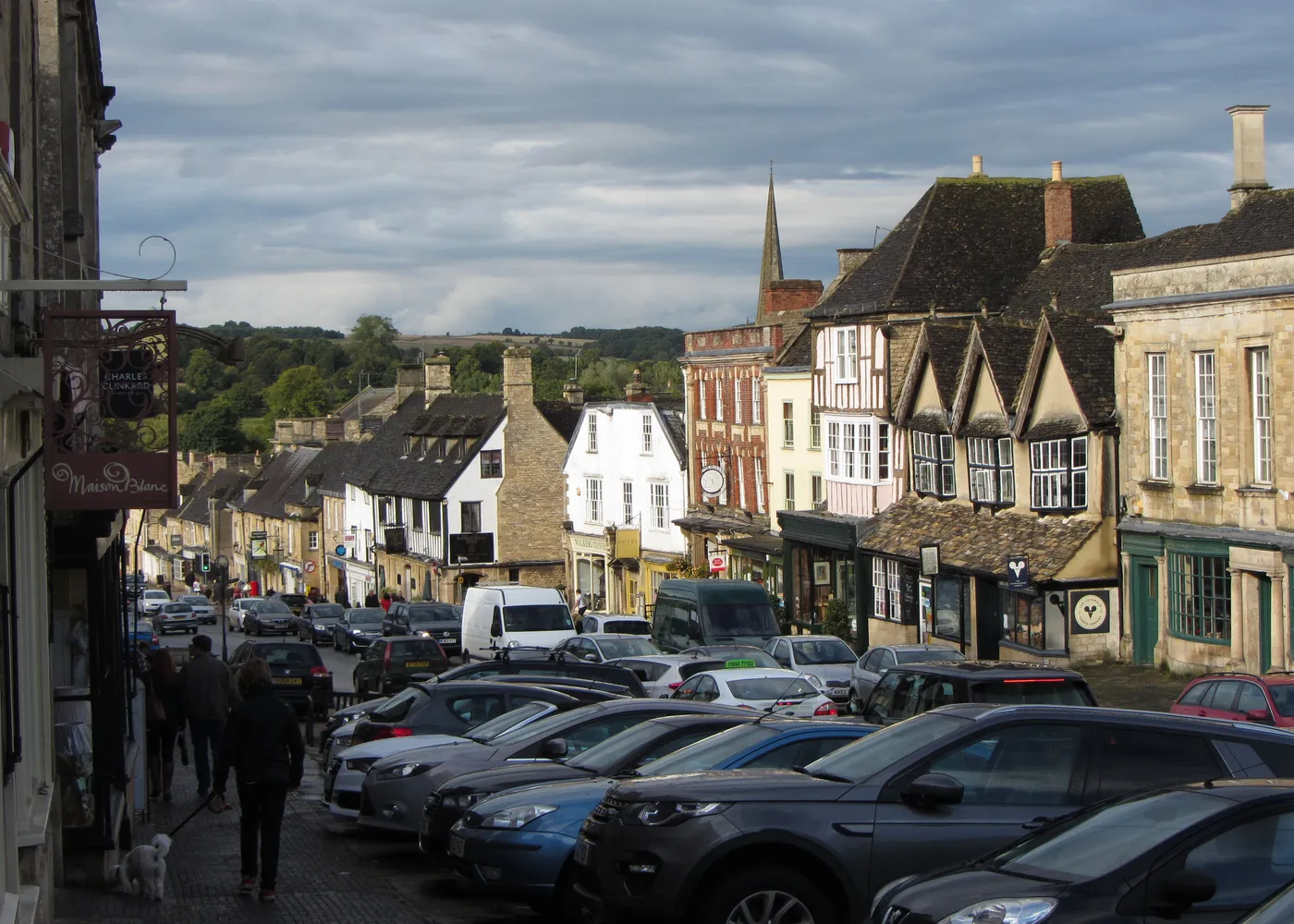 Burford High Street running downhill between stone buildings, with parked cars