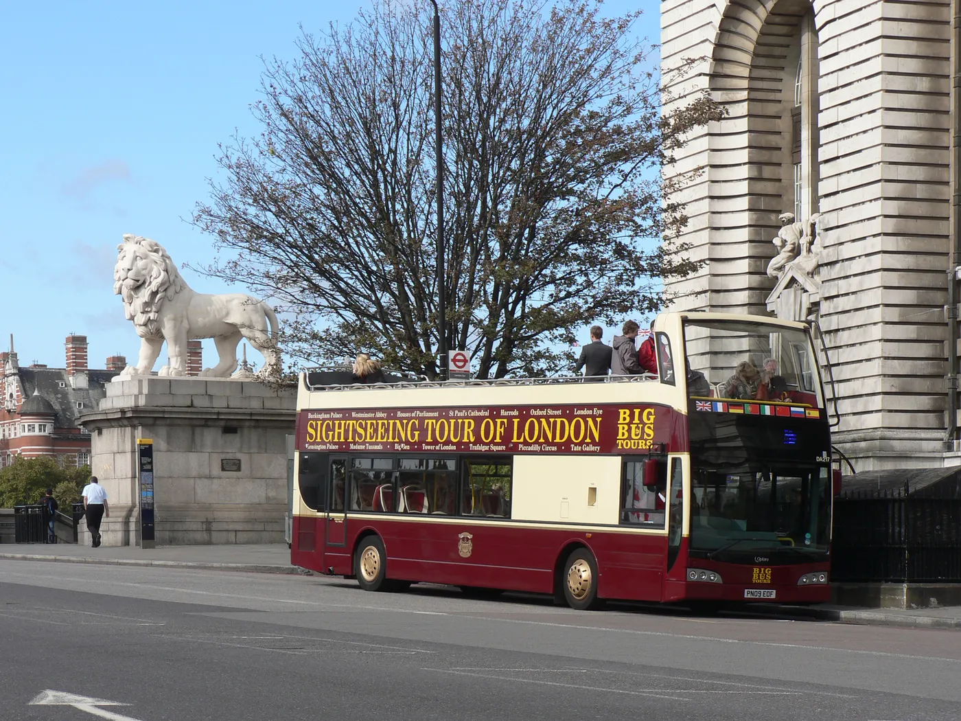 Open-top sightseeing bus crossing Westminster Bridge beside the South Bank Lion