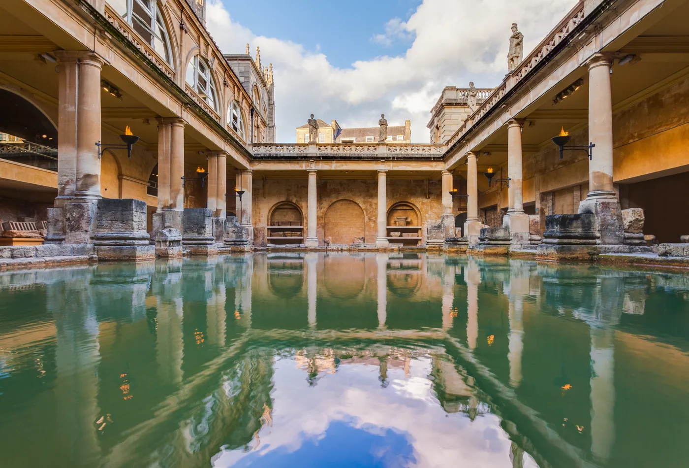 The green water of the Great Bath surrounded by columns and statues, with Bath Abbey behind